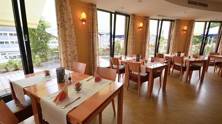 Ein einladendes Restaurant mit Holzstühlen und Tischen. Große Fenster bieten einen Blick auf den Außenbereich.