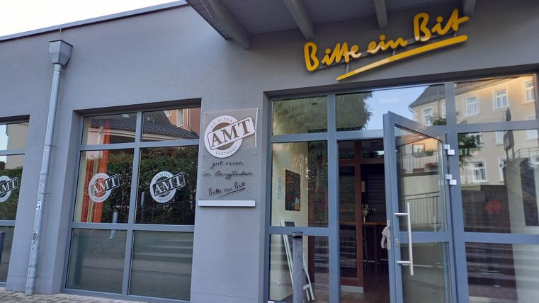 Een modern gebouw met grote ramen en een uitnodigende ingang. Het bord toont de naam "Bitte ein Bit" en het logo "AMT".