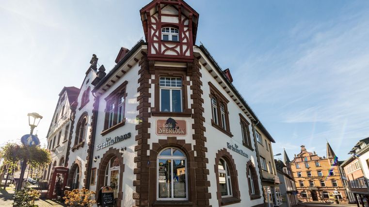 Historisches Gebäude mit Café Sherlock und Kriminalhaus an einer Straßenecke, blauer Himmel im Hintergrund.