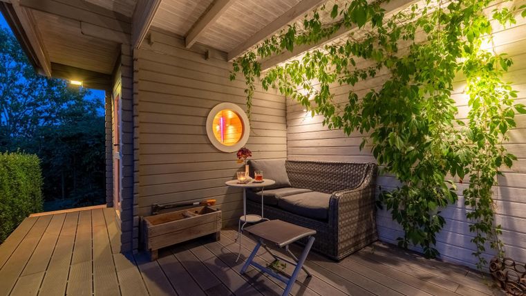 Ein gemütlicher Außenbereich mit einem Sofa und einem kleinen Tisch. Die Wände sind mit Pflanzen dekoriert und sanft beleuchtet.