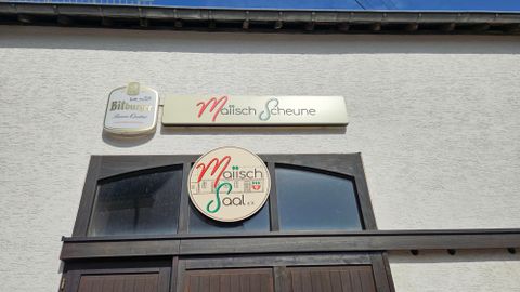 Un bâtiment avec deux panneaux. L'un indique "Maitisch Scheune" et l'autre "Maitisch Saal".