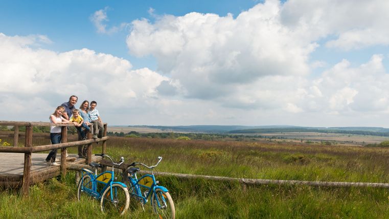 Familie auf Holzplattform im Hohen Venn mit Fahrrädern im Vordergrund.