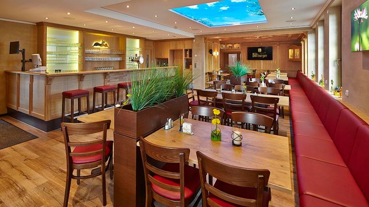 Ein gemütliches Restaurant mit Holztischen und roten Bänken. Der Raum ist hell und hat eine Decke mit Himmel und Wolken.