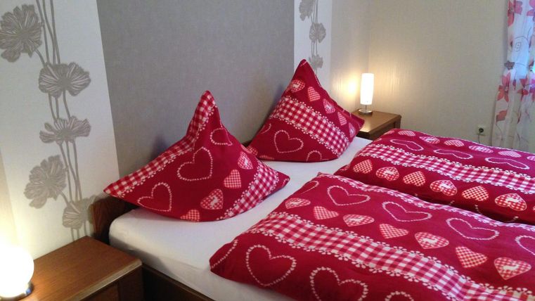 Ein gemütliches Schlafzimmer mit einem Doppelbett und dekorativen Kissen in Rot mit Herzen. Sanfte Beleuchtung schafft eine einladende Atmosphäre.