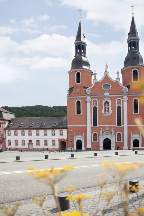 Une église magnifique avec deux tours et une façade impressionnante se dresse au premier plan. À l'arrière-plan, on aperçoit des collines douces et un ciel bleu.