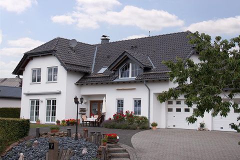 Ein schönes, modernes Haus mit einem grauen Dach und weißen Wänden. Der Garten ist gut gepflegt und mit Blumen und Sträuchern geschmückt.