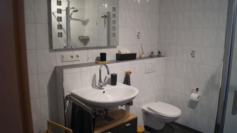 Ein modernes Badezimmer mit einer weißen Waschbecken und einer Dusche. Die Wände sind gefliest und der Raum wirkt hell und sauber.