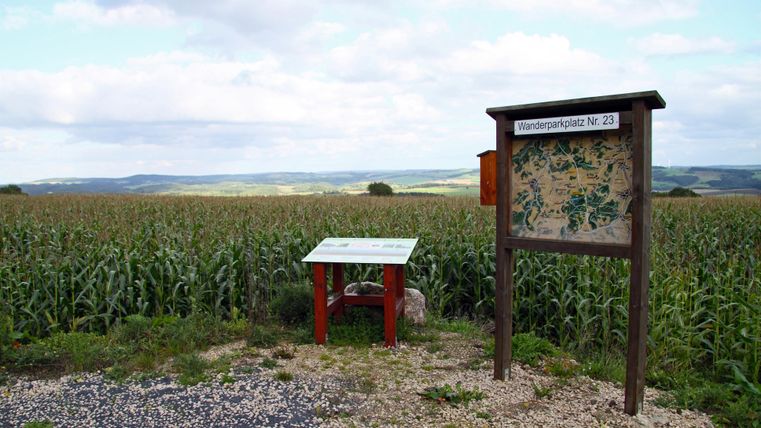 Un stand d'information dans un champ de maïs. À l'arrière-plan, on peut voir de douces collines et un ciel nuageux.