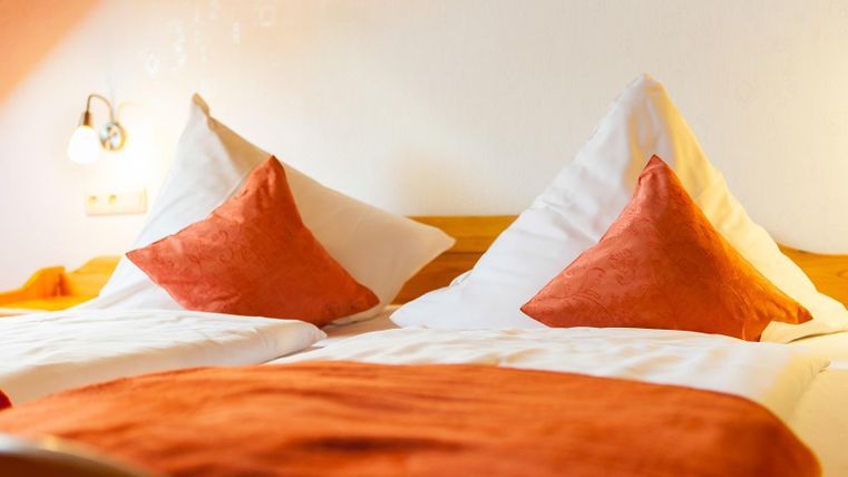 Ein gemütliches Schlafzimmer mit zwei betten und orangefarbenen Kissen. Sanfte Beleuchtung schafft eine entspannte Atmosphäre.