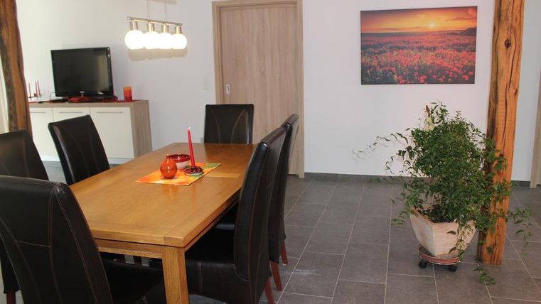 Ein modernes Esszimmer mit einem großen Holztisch und schwarzen Stühlen. An der Wand hängt ein Bild einer blühenden Landschaft bei Sonnenuntergang.