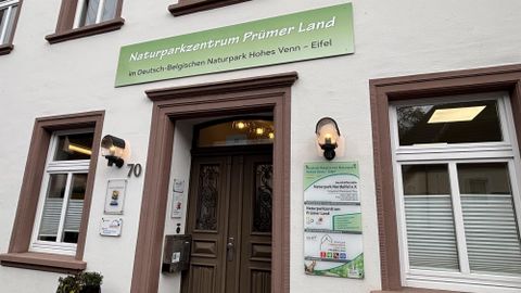 The image shows the nature park center Prümer Land with an inviting entrance area. Above the door is a sign with the name of the center and information about the nature parks in the region.