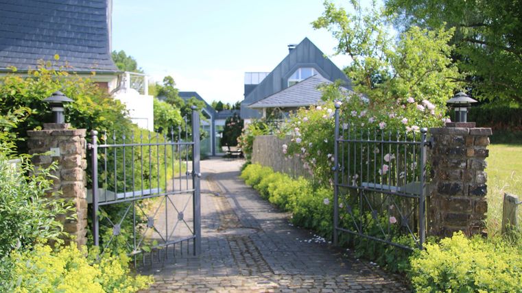 Ein schöner Eingang mit einem offenen Tor und grünen Pflanzen. Im Hintergrund sind Häuser zu sehen.