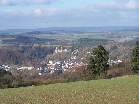 Eine malerische Landschaft mit sanften Hügeln und einem kleinen Dorf im Tal. Im Hintergrund ist eine alte Burg sichtbar.