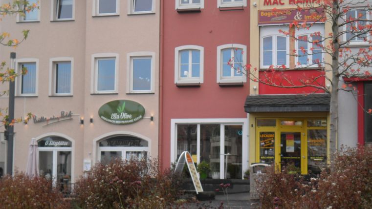 Eine Reihe von Gebäuden in einer Stadt. Einige Geschäfte sind sichtbar, darunter ein Restaurant und ein Imbiss.