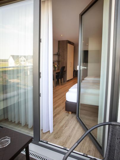 Ein Blick auf einen Balkon mit Blick auf ein helles Zimmer. Die Türen sind weit geöffnet und der Boden ist aus Holz.