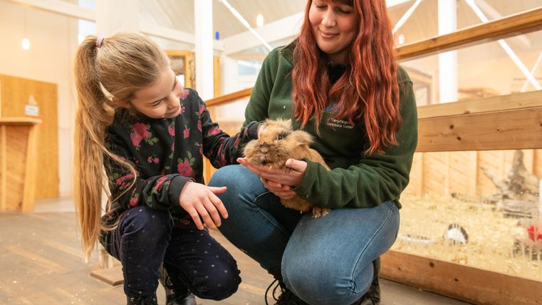 Une fille et une femme tiennent un lapin dans un jardin zoologique. Les deux sourient et montrent leur joie en interagissant avec l'animal.