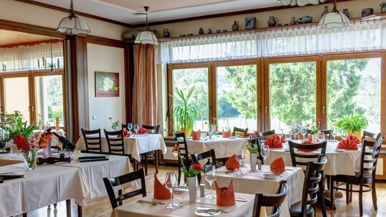 Ein elegantes Restaurant mit mehreren gedeckten Tischen und Blick auf den Garten. Große Fenster sorgen für viel Tageslicht und eine einladende Atmosphäre.