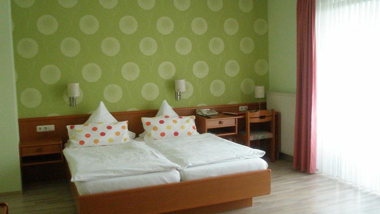 Ein modernes Schlafzimmer mit zwei Betten und bunten Kissen. Die Wände sind mit grünen Punkten dekoriert und das Zimmer hat große Fenster mit viel Tageslicht.