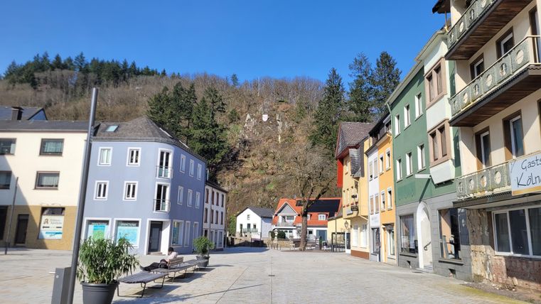 A quiet place with colorful buildings and a clear blue sky. In the background, wooded hills are visible.