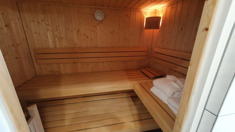 Eine gemütliche Sauna mit Holzverkleidung und bequemen Bänken. Im Hintergrund sieht man eine weiche Beleuchtung und ein Handtuch.